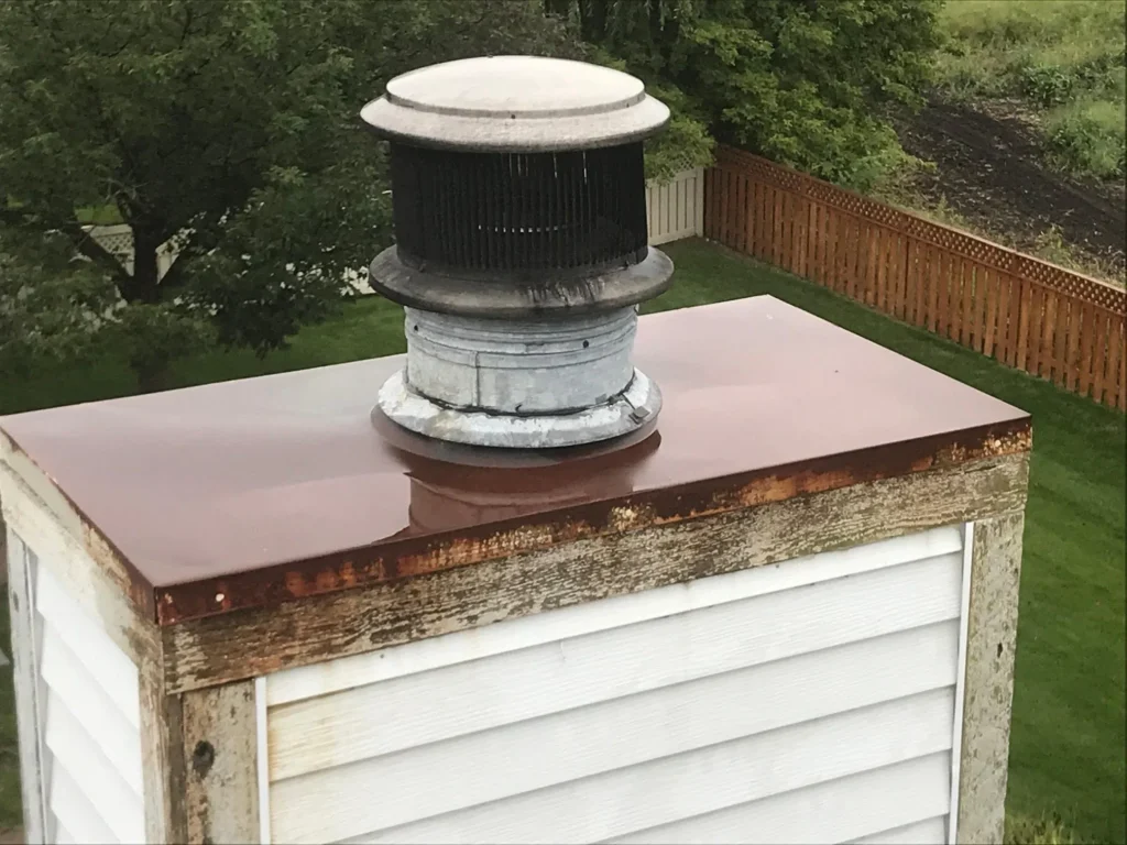 Real photo of a rusted galvanized chase cover with rust streaks on the siding